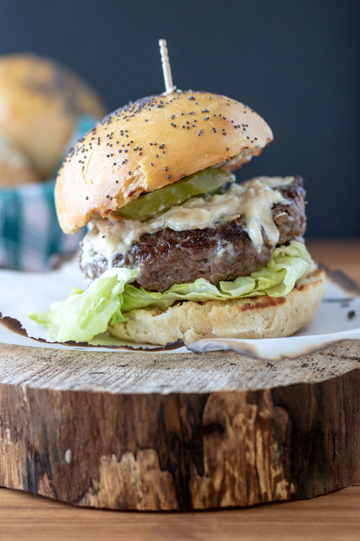 Pickle topped brie burger on poppy seed bun on log round