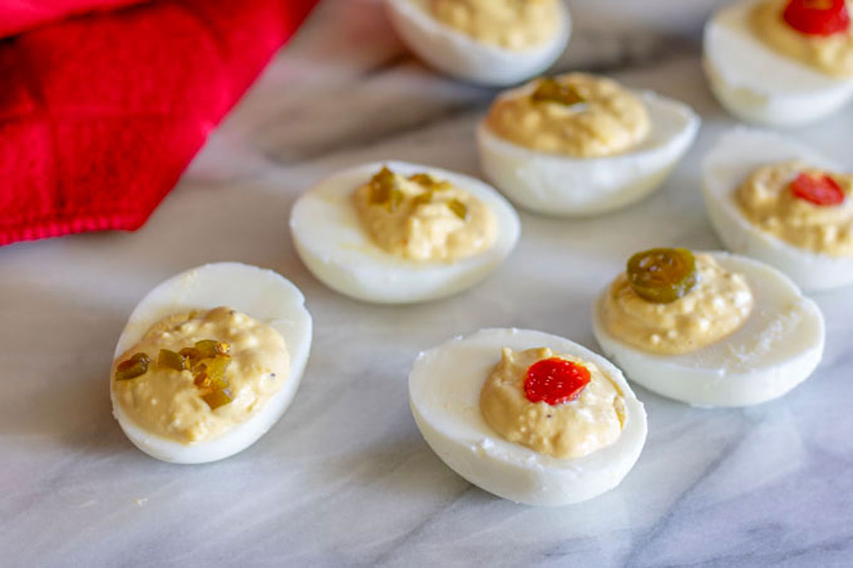 Red and green pepper topped spicy deviled eggs on marble board.