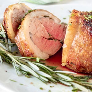 sliced lamb loin on white platter with fresh herbs