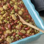 Blue cassrole dish filled with multiple colored and sized baked beans.