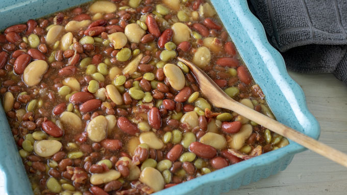 Casserole full of four bean baked beans with wooden spoon.
