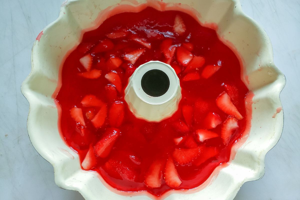 Strawberries added to the strawberry jello in a mold.