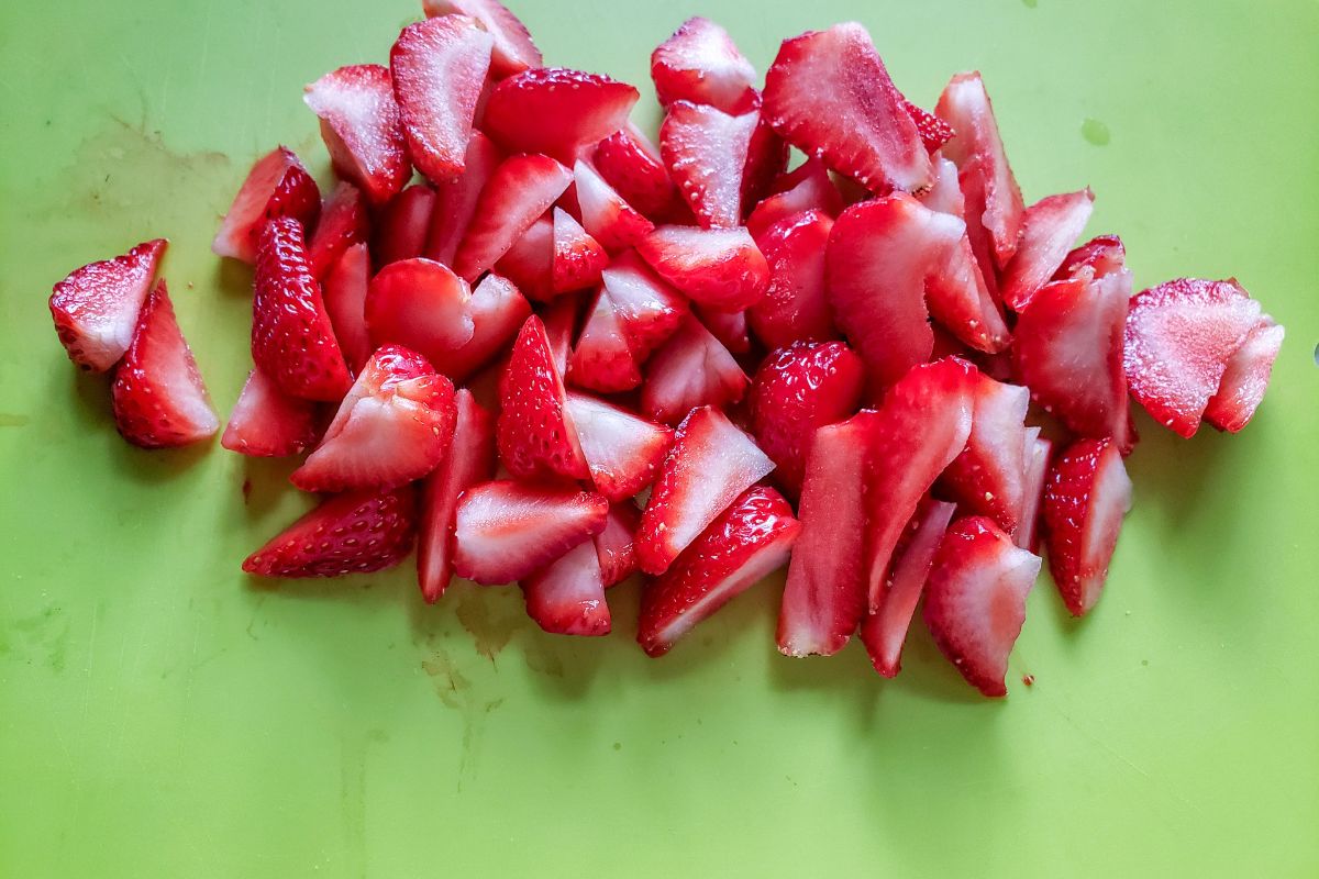 Strawberries sliced on a green cutting board.