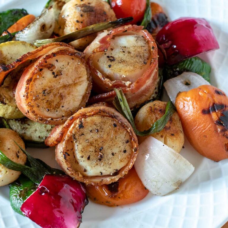 Grilled bacon-wrapped scallops on a bed of colorful grilled vegetables.
