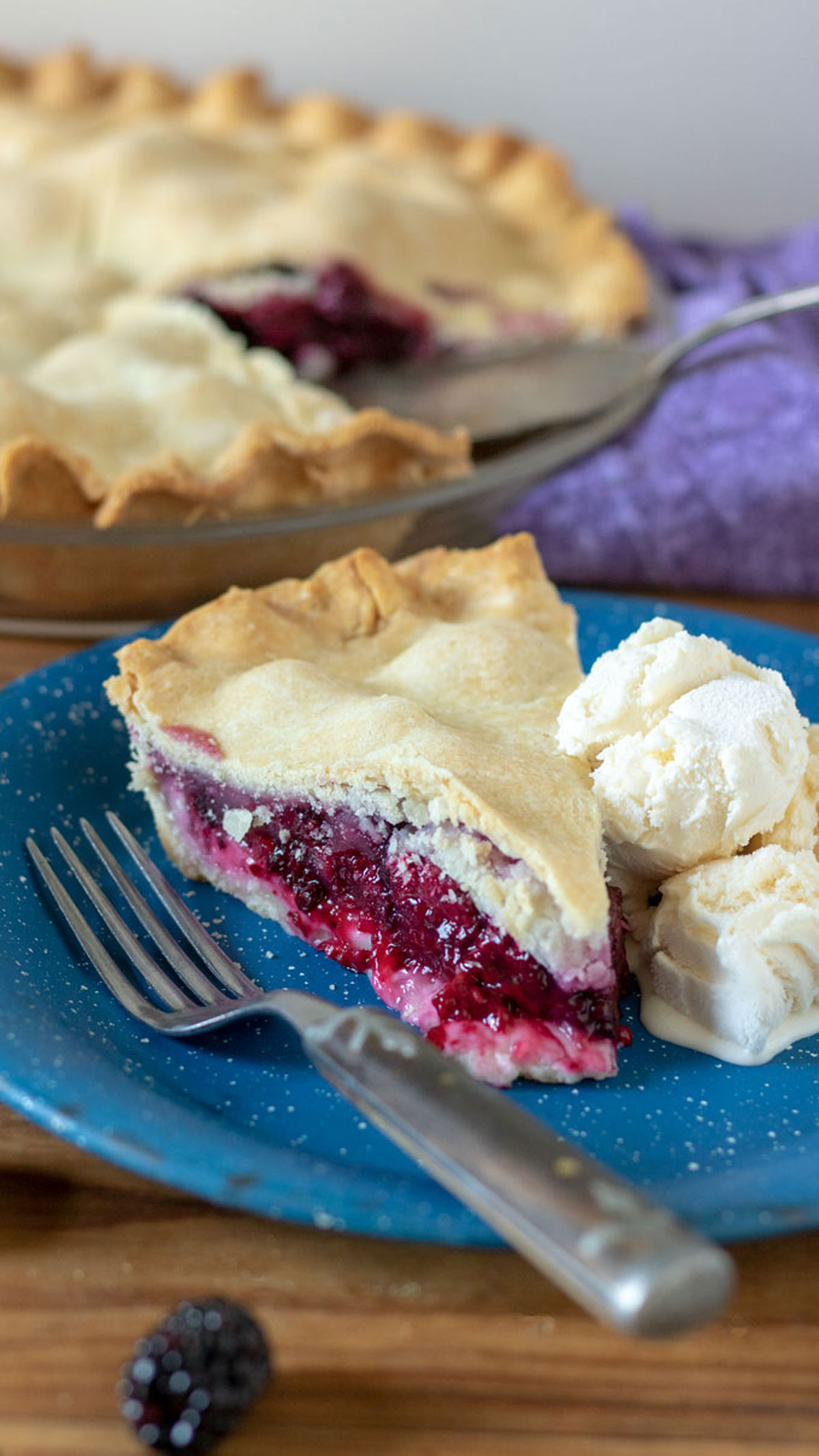 Slice of blackberry pie on vintage blue plate with ice cream