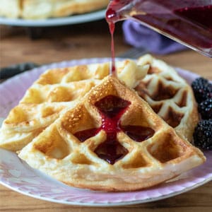 3 waffles on pink plate with blackberry syrup pouring