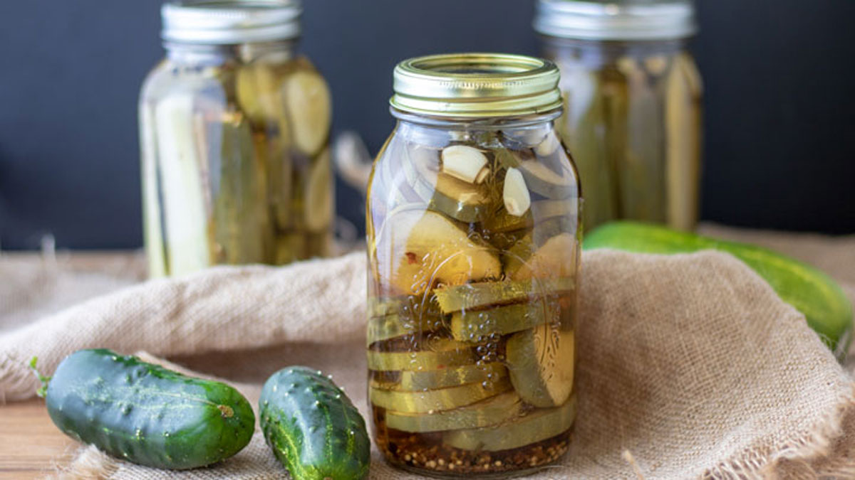 Sliced pickles in jars with fresh cucumbers in photo