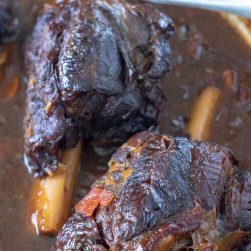Close up of venison shanks in red wine sauce in Dutch oven.