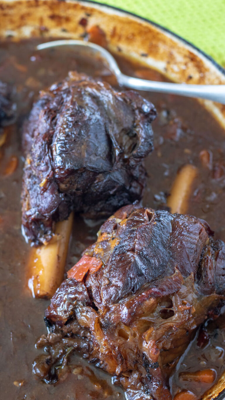 Close up of venison shanks in red wine sauce in Dutch oven.
