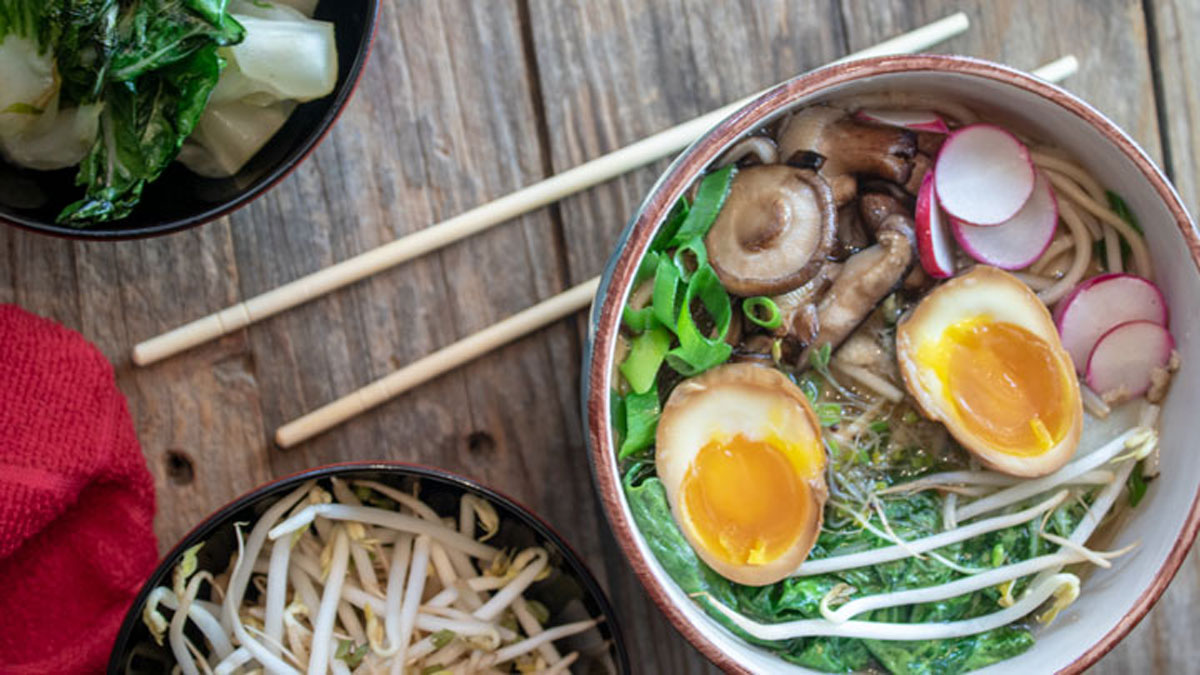 Chicken ramen in bowl with bowls of vegetables.