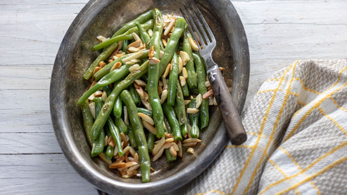 Sauteed green beans and almonds on silver dish with wooden spoon.