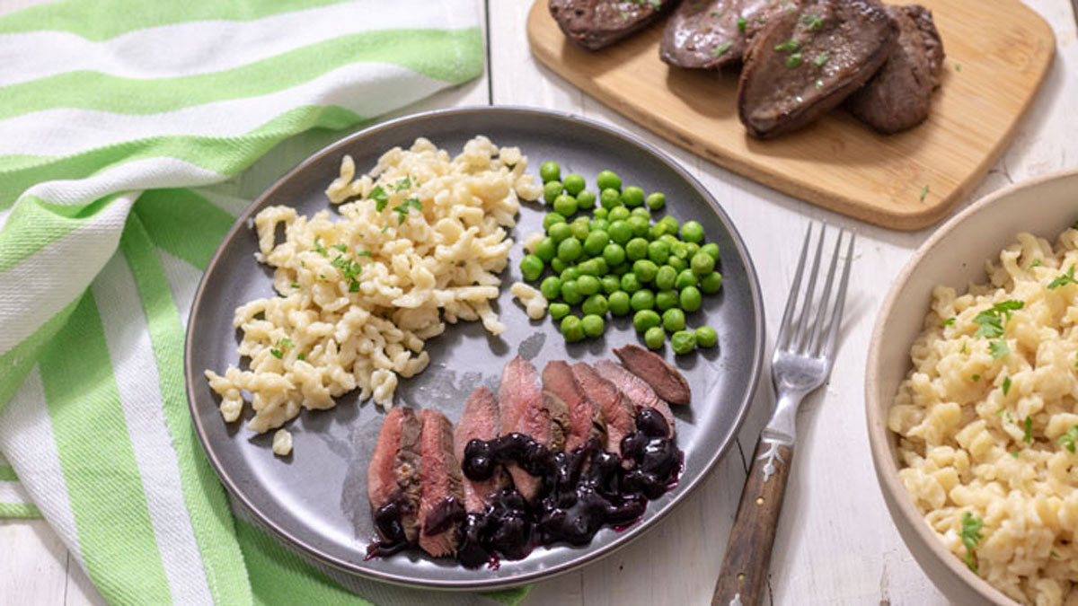 Spaetzle served with duck and peas on grey plate.