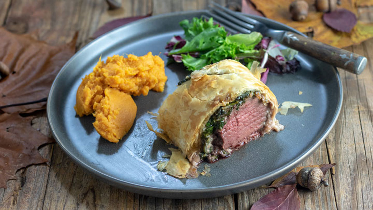 Slice of venison wellington with sides on gray plate.