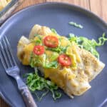 Turkey enchiladas verdes on gray plate with colorful garnishes