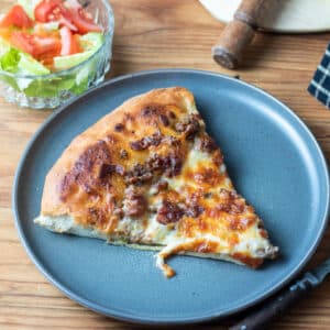 slice of cheeseburger pizza on grey plate.