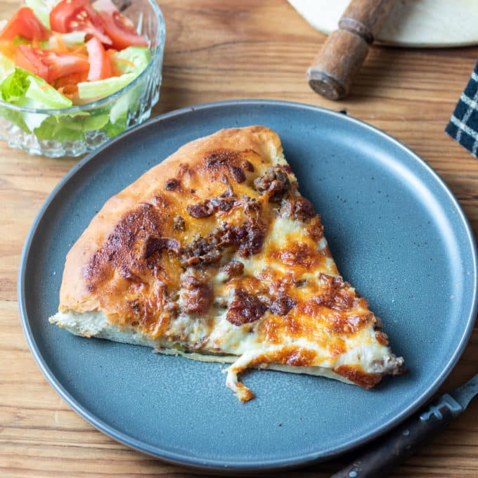 slice of cheeseburger pizza on grey plate.