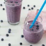 Blueberry smoothie in rounded glass with blue straw.