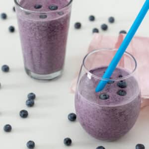 Blueberry smoothie in rounded glass with blue straw.