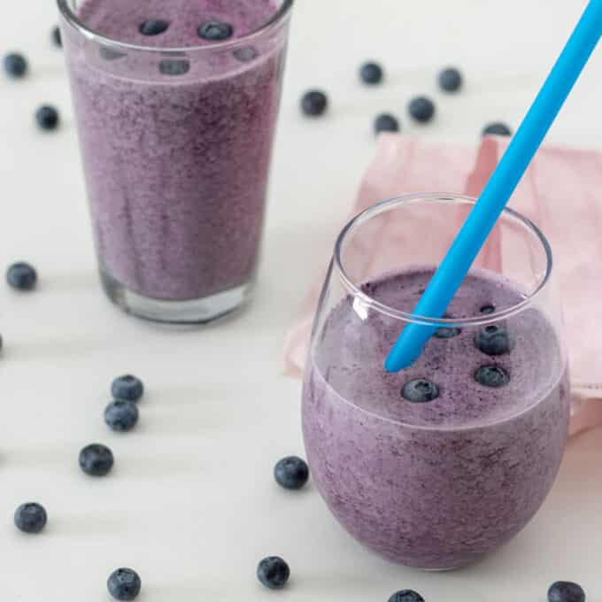 Blueberry smoothie in rounded glass with blue straw.