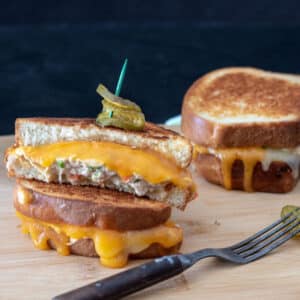 Tuna melt with dripping cheese and pickle garnish.