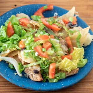Chicken nachos on blue pewter plate topped with lettuce and tomatoes.