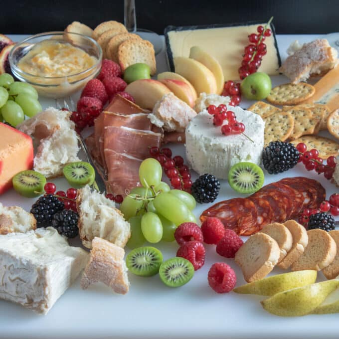 Grazing platter with cheese, sliced meats and colorful fruits.