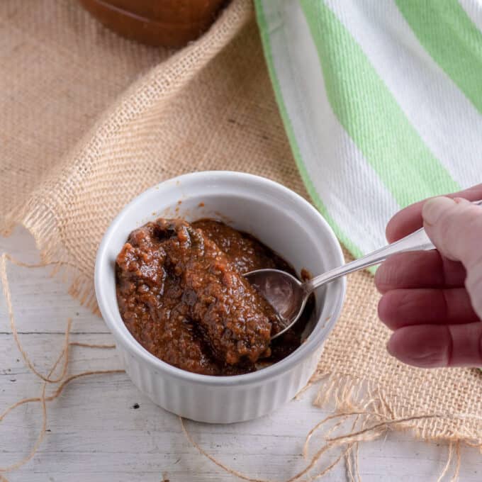Chipotle in Adobo Sauce in white bowl with hand scooping sauce out with spoon. in white bowl.