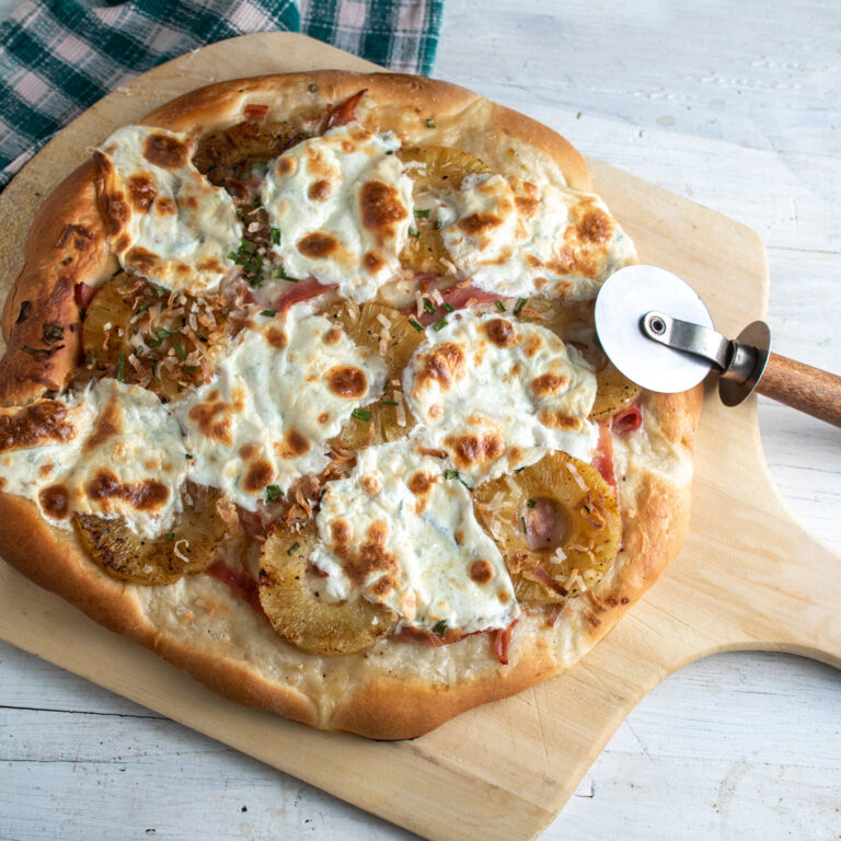 Ham and pineapple pizza on a wooden pizza peel.