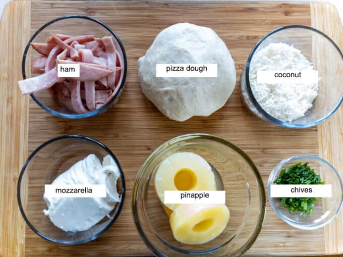 Ingredients for pizza- pizza dough, ham, coconut, mozzarella, pineapple, chives.