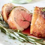 Sliced lamb loin, medium rare on white platter with fresh rosemary.