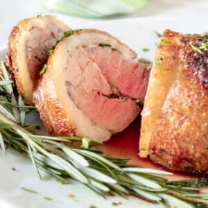 Sliced lamb loin, medium rare on white platter with fresh rosemary.