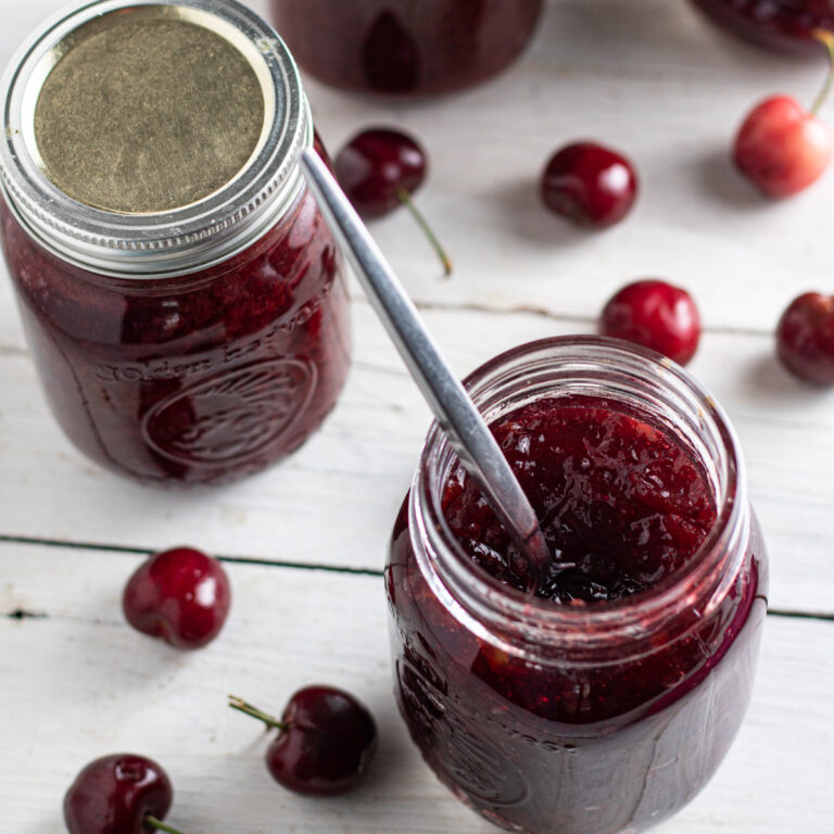 Spoon resting inside an opened jar of cherry jam.