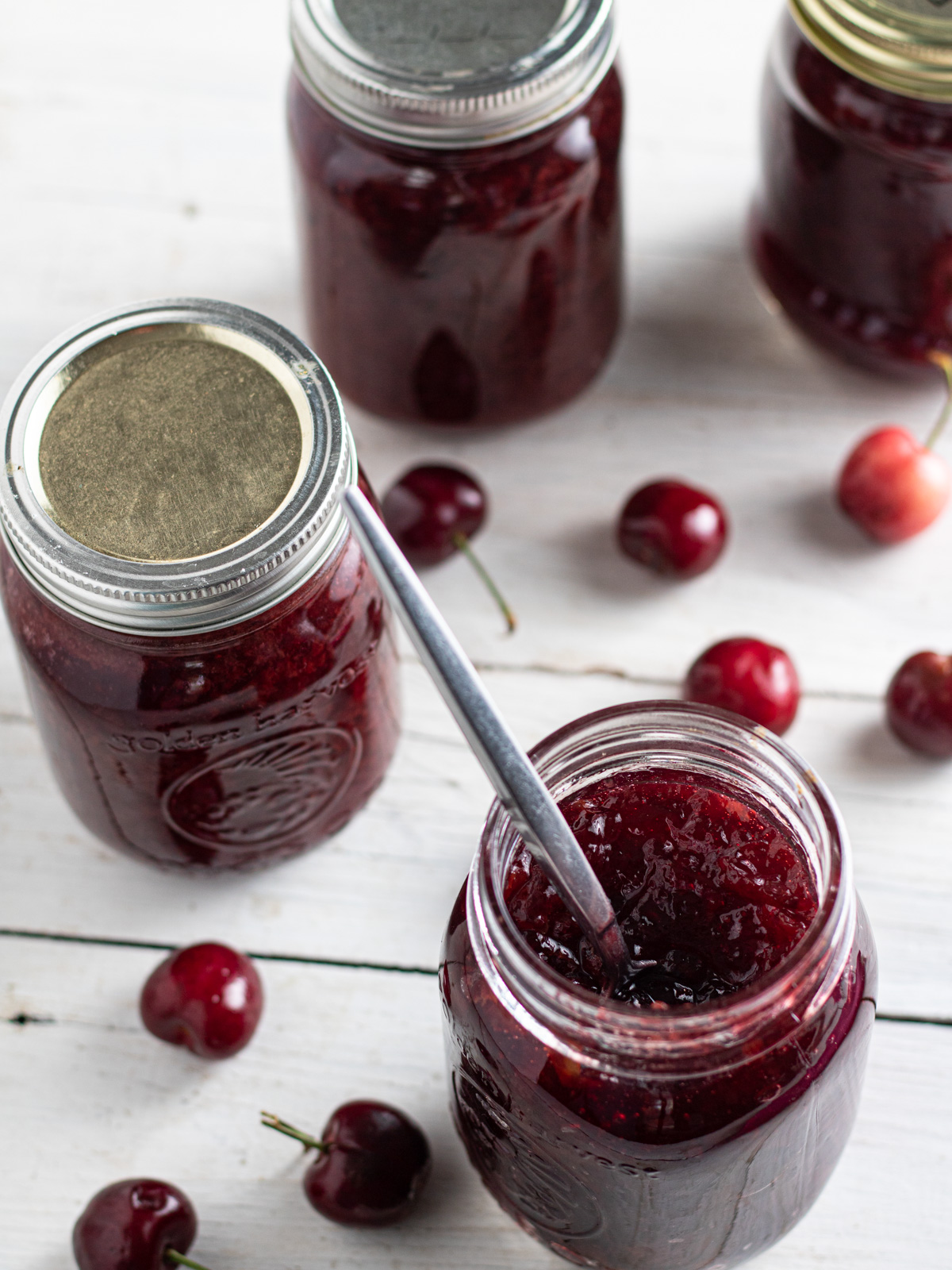 Jars of cherry jam, one with spoon sticking out.