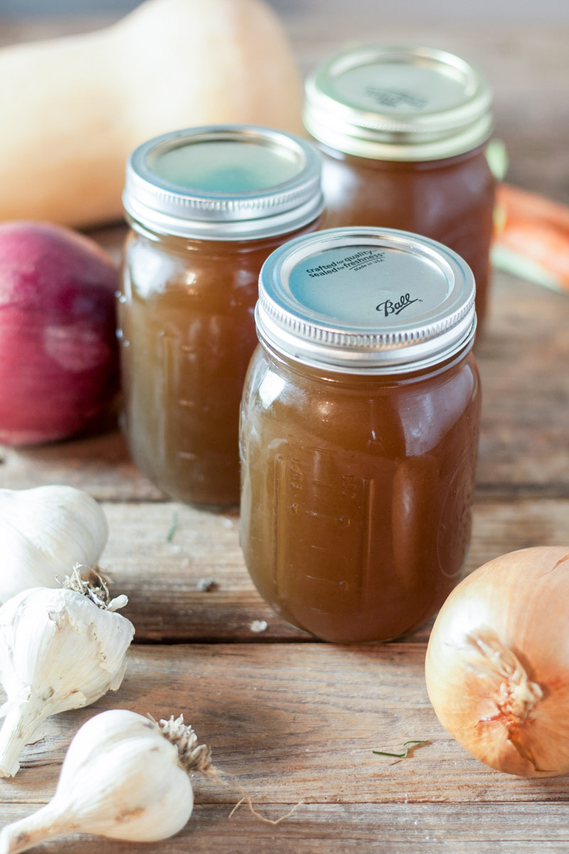 Jars of canned vegetable stock with raw vegetables in the shot.