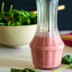 Rhubarb vinaigrette in cruet with salad in background.