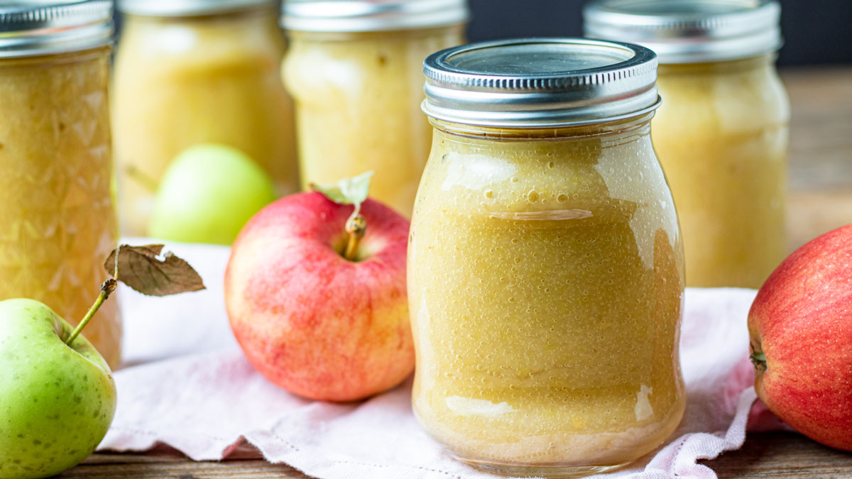 Five jars of applesauce with colorful apples.