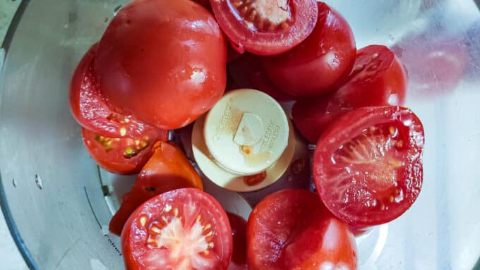 Halved tomatoes in food processor container.