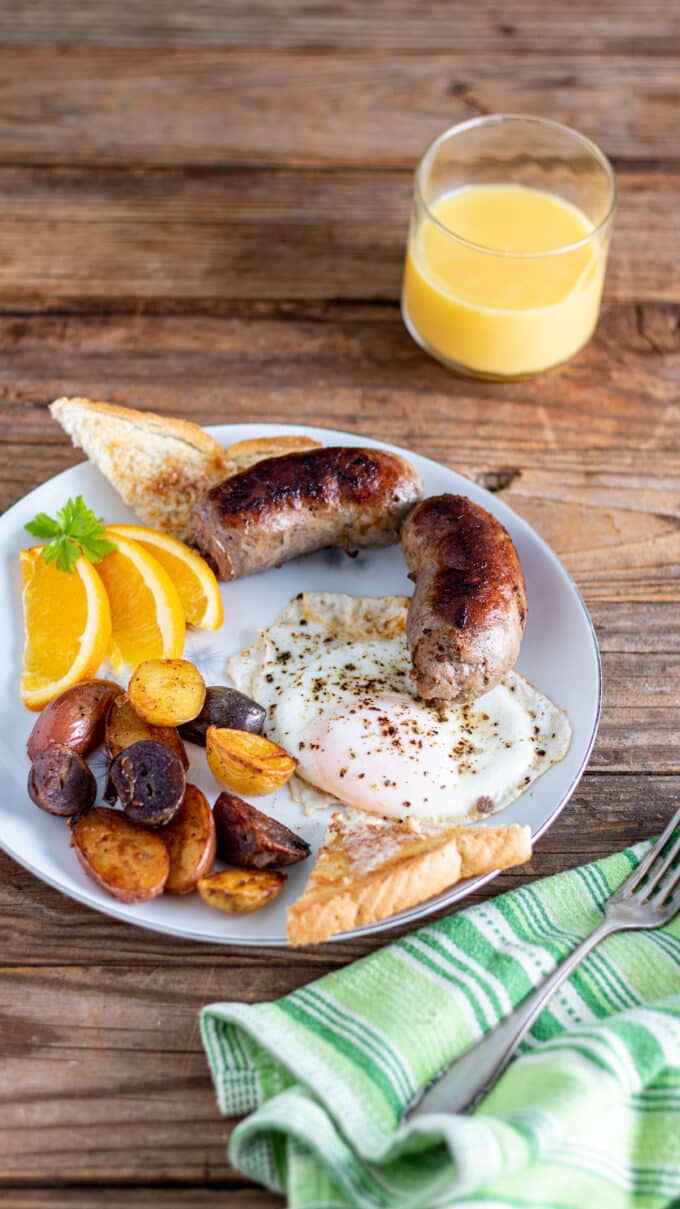 Eggs potatoes and sausage with toast and garnished with orange slices.