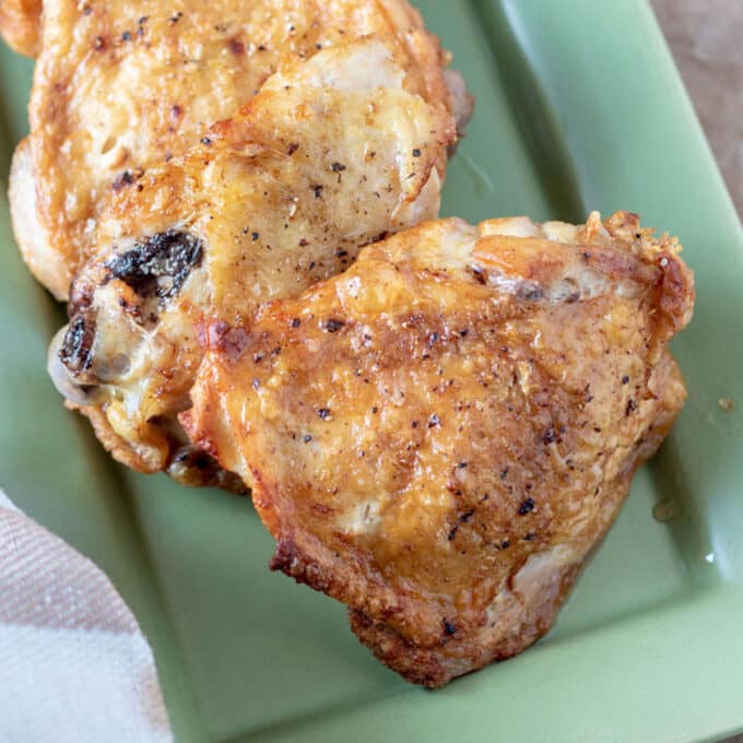 crispy chicken thighs on green platter.