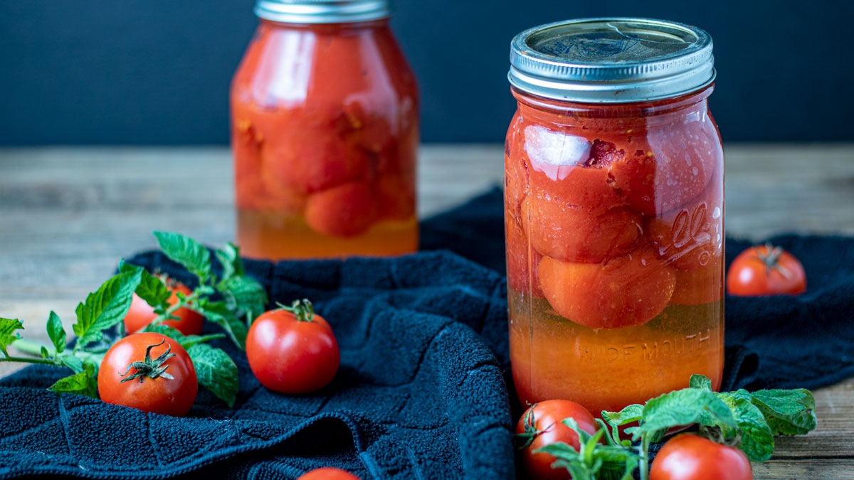 Canned tomatoes with fresh tomatoes and leaves.
