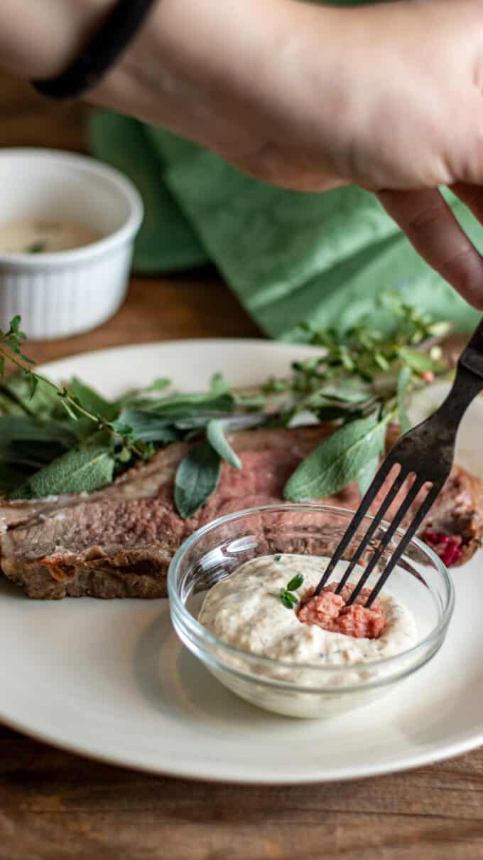 Fork dipping piece of beef into horseradish sauce.