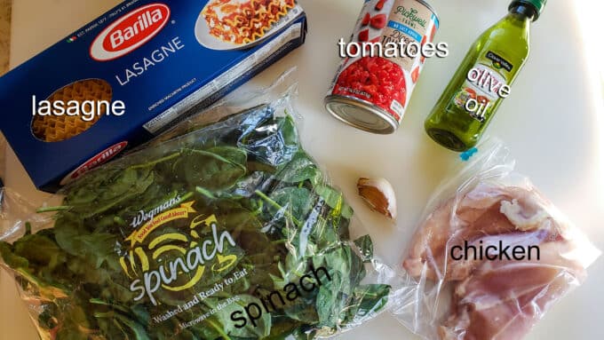 Ingredients for lasagna; pasta, tomatoes, olive oil, spinach chicken, garlic.