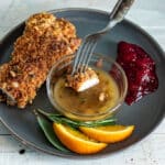 Fork dipping piece of turkey schnitzel in orange sauce.