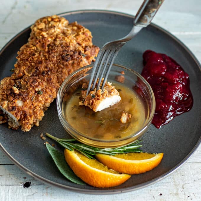 Fork dipping piece of turkey schnitzel in orange sauce.