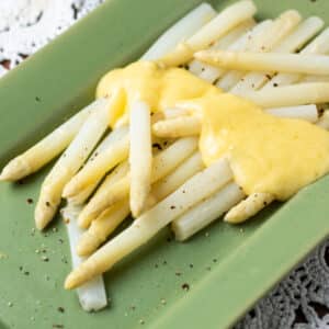 White asparagus on green platter with Hollandaise sauce drizzle.