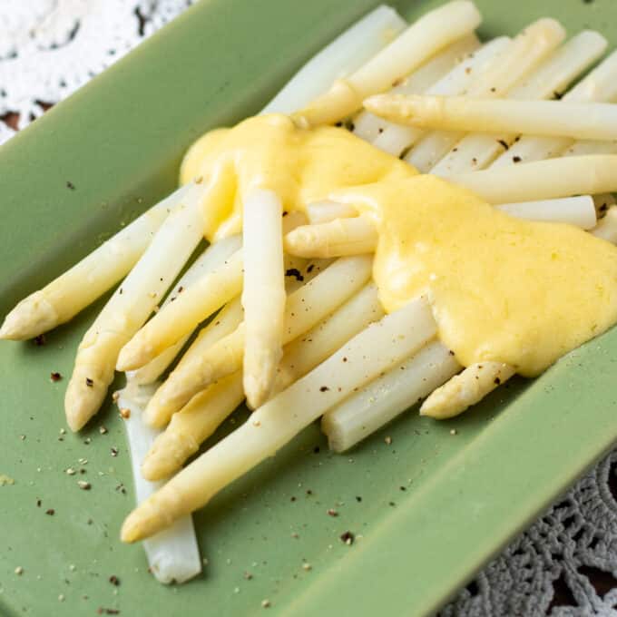 White asparagus on green platter with Hollandaise sauce drizzle.