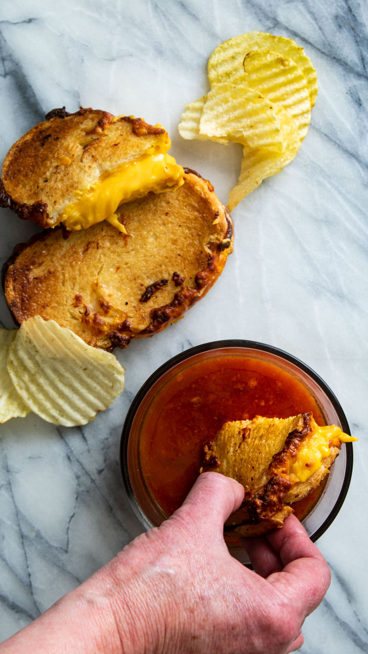 Woman's hand dipping a piece of grilled cheese in tomato soup.