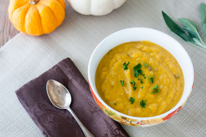 Butternut Squash Soup in a bowl with miniature pumpkin gourds in the background.