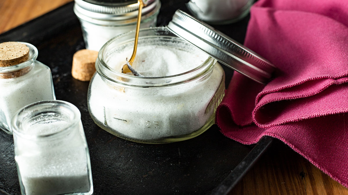 Gold spoon scooping out sugar from jar.