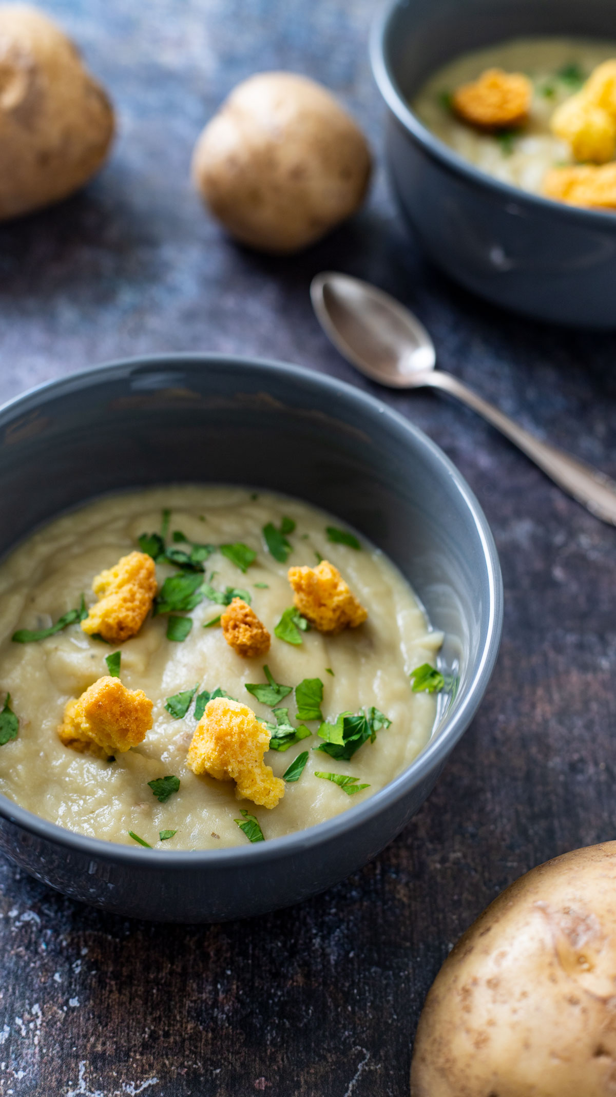 Bowl of instant pot potato leek soup in gray bowl with potatoes on the side.